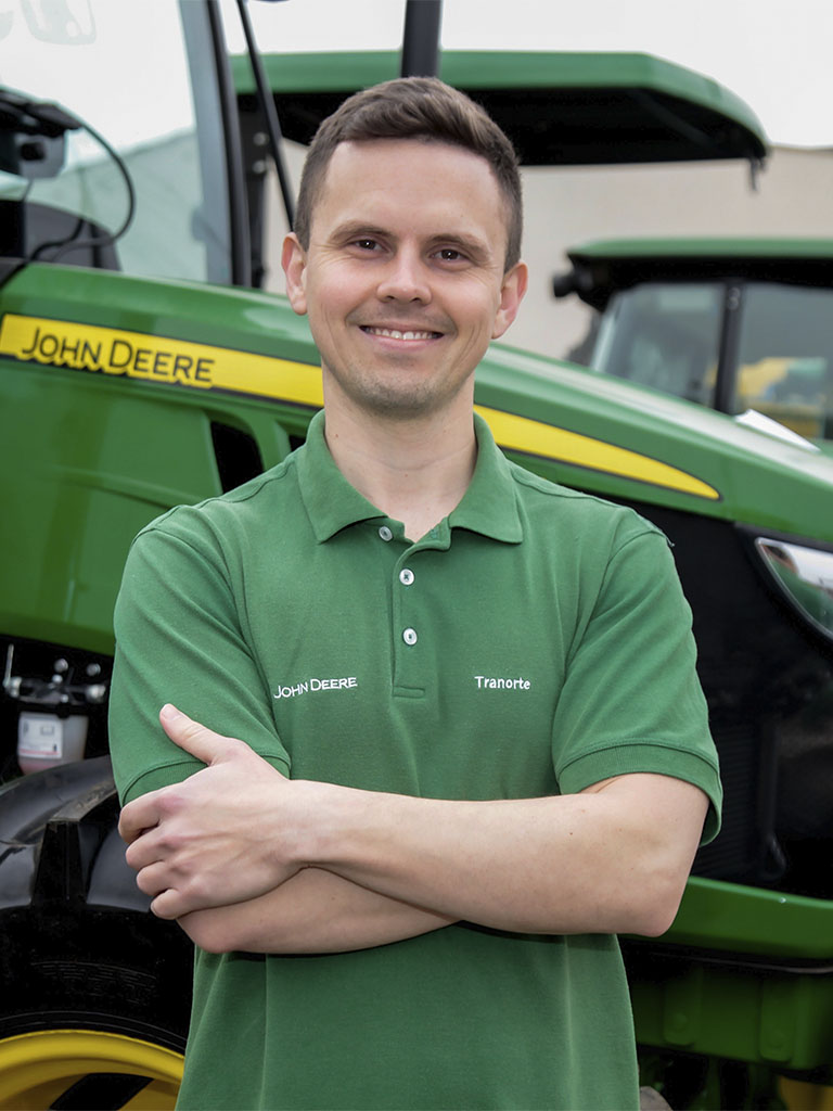foto mostrando funcionario de braços cruzados com trator John Deere atras