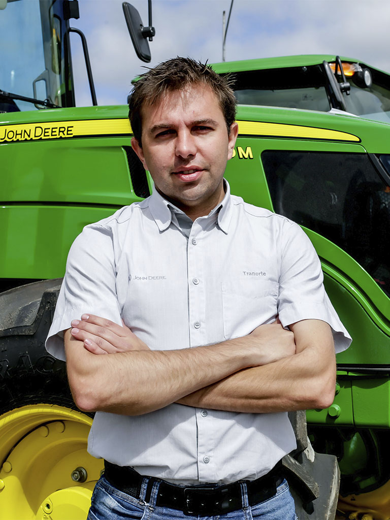 foto mostrando funcionario de braços cruzados com trator John Deere atras