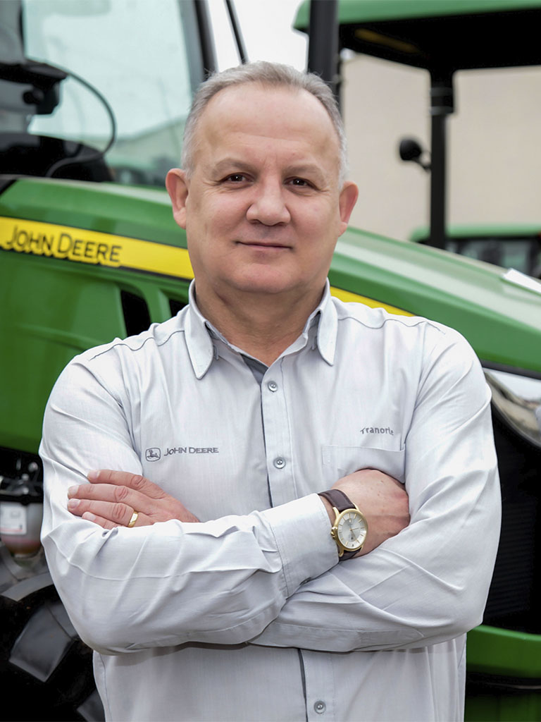 foto mostrando funcionario de braços cruzados com trator John Deere atras