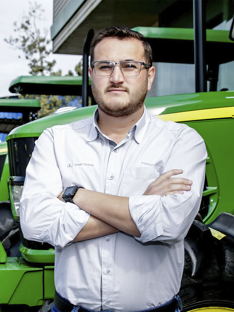 foto mostrando funcionario de braços cruzados com trator John Deere atras