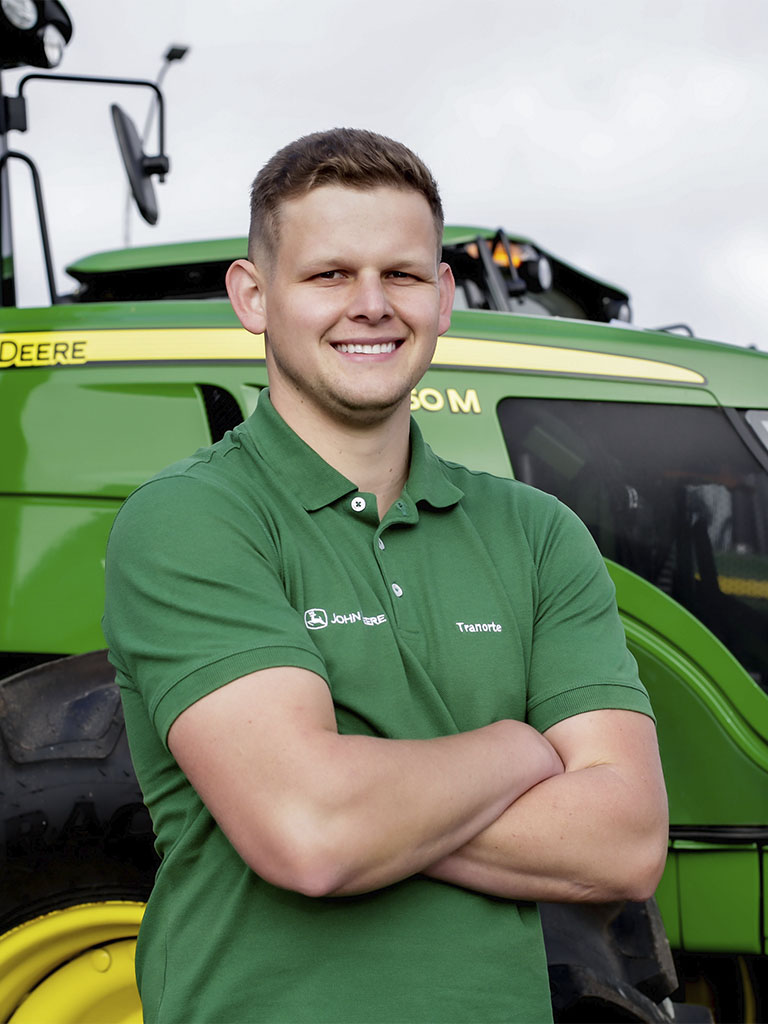 foto mostrando funcionario de braços cruzados com trator John Deere atras