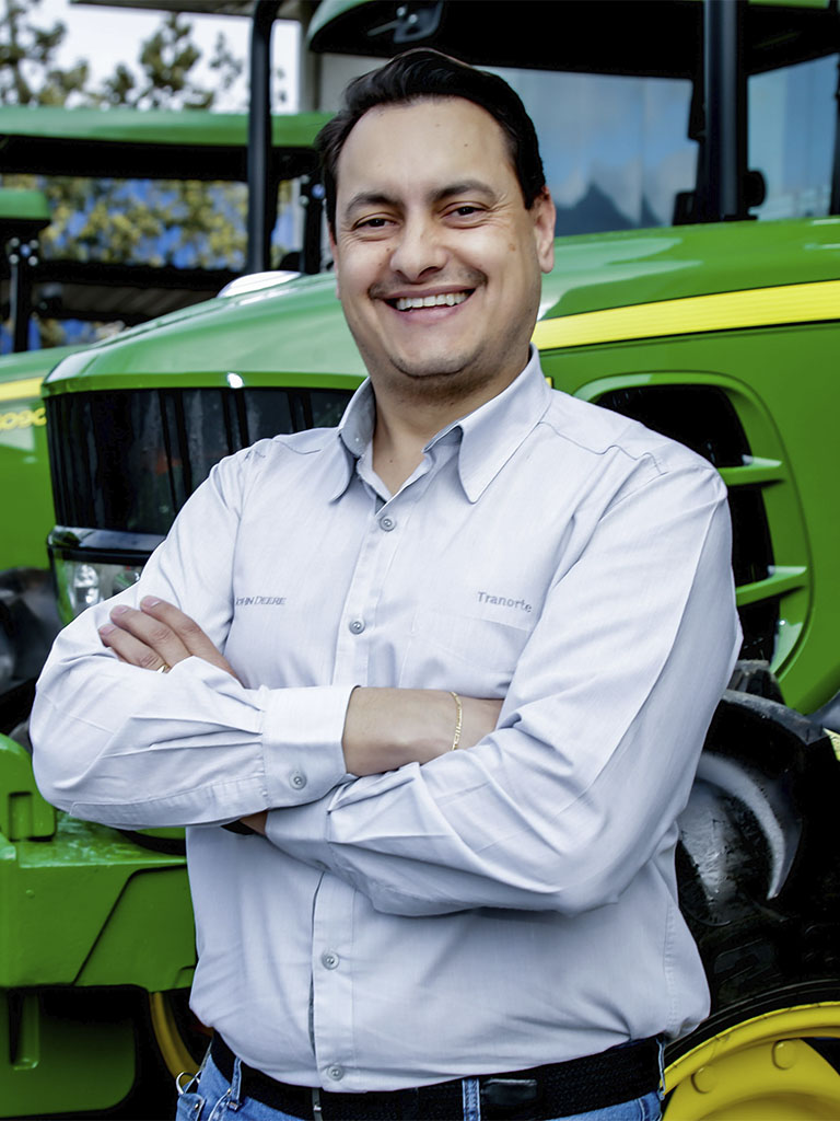 foto mostrando funcionario de braços cruzados com trator John Deere atras