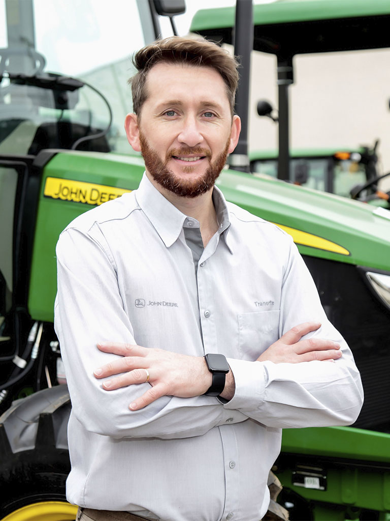foto mostrando funcionario de braços cruzados com trator John Deere atras
