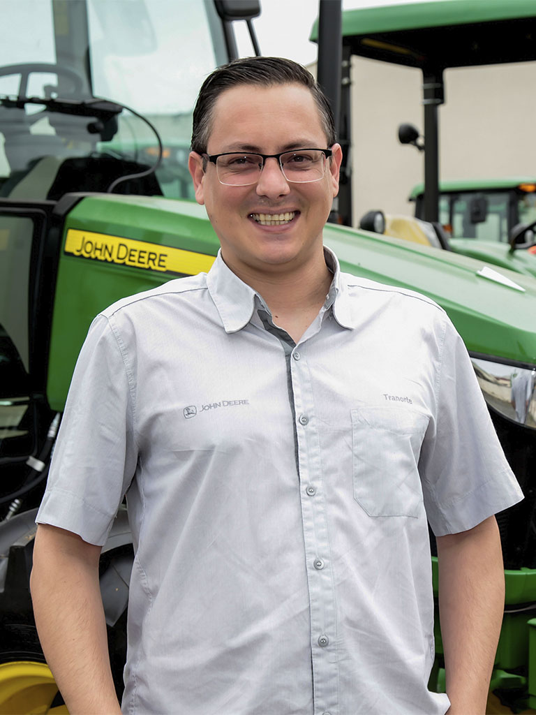 foto mostrando funcionario de braços cruzados com trator John Deere atras