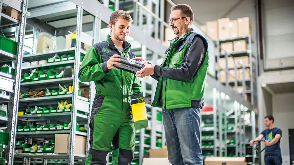 homem apresentando produto John Deere em frente a pratelheiras