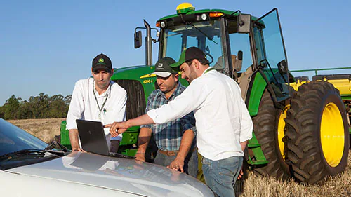 tres homens conversando em frente a um trator John Deere